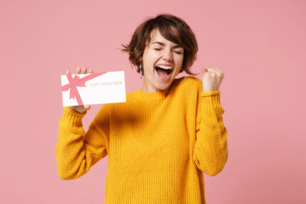 Excited woman holding gift voucher on pink background