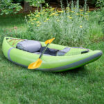 Green inflatable kayak with yellow paddle on grass